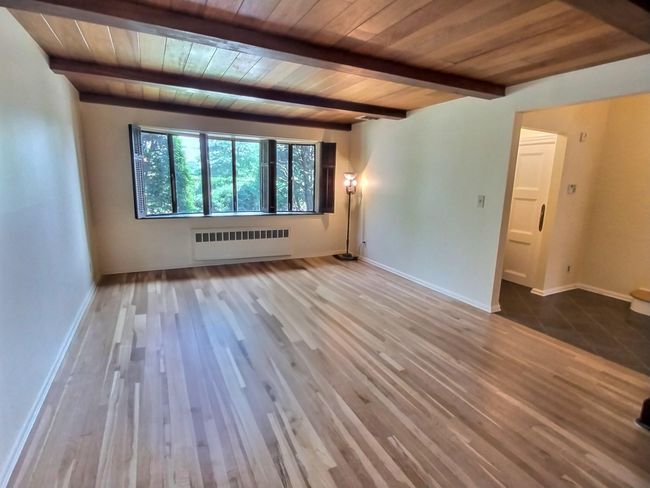 Unfurnished room with radiator, wood ceiling with exposed beams, wood finished floors, and baseboards | Image 8