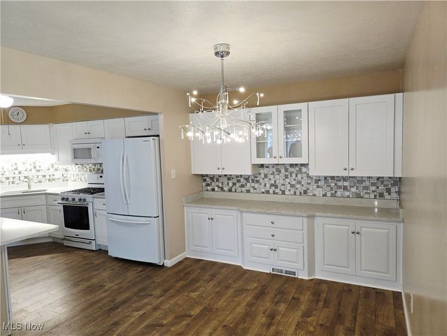 Kitchen with white appliances, decorative backsplash, white cabinets, and glass insert cabinets | Image 10