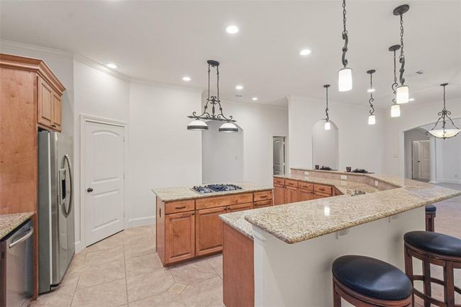 This chef's kitchen features stainless steel appliances, ample cabinetry, granite countertops, and a large wrap-around breakfast bar. The kicthen is very well-lit with a combination of pendant and recessed lighting with dimmers. | Image 20