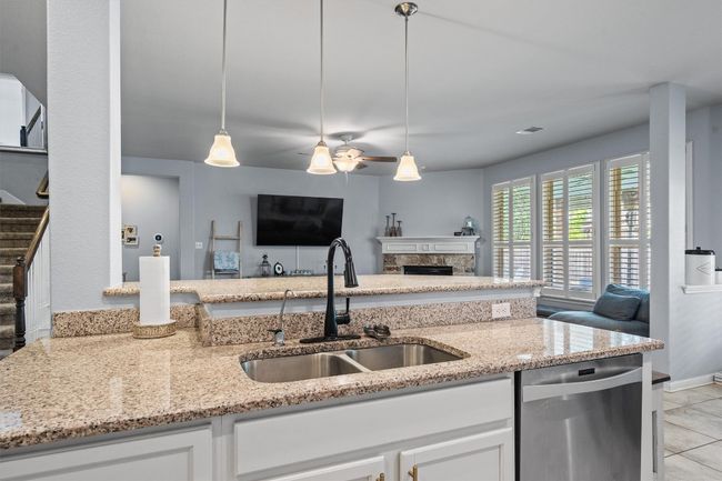 Kitchen with stainless steel dishwasher, a sink, open floor plan, light stone counters, and white cabinets | Image 16