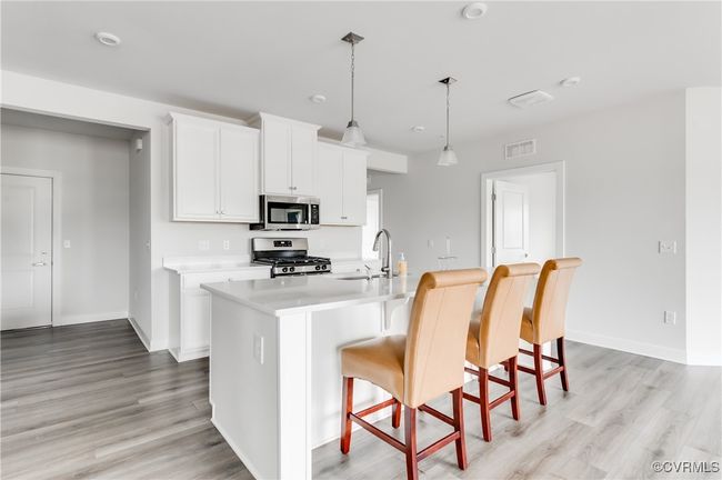 Kitchen featuring appliances with stainless steel finishes, light countertops, a breakfast bar area, a center island with sink, and light wood finished floors | Image 12