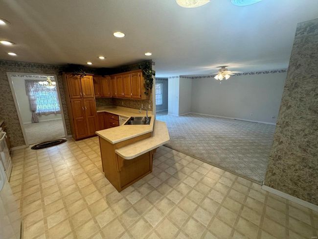 Kitchen featuring a breakfast bar, sink, ceiling fan with notable chandelier, kitchen peninsula, and light colored carpet | Image 5