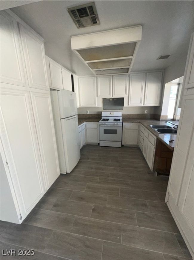 Kitchen featuring range, refrigerator, white cabinetry, a sink, and dark countertops | Image 6