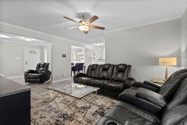 Living room featuring crown molding, baseboards, a textured ceiling, light wood-style flooring, and ceiling fan with notable chandelier | Image 7