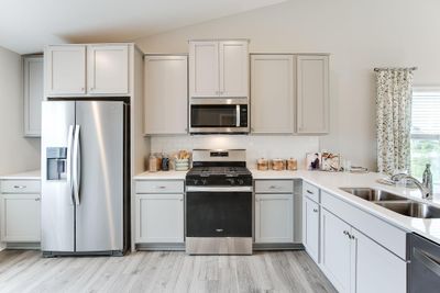 Kitchen shown with white cabinets, gas oven/range, microwave over cooktop, and quartz countertops. Photos is of model home. Colors and options may vary. Ask Sales Agent for details. | Image 3