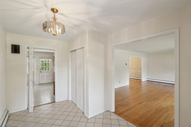 Hall with baseboards, an inviting chandelier, a baseboard radiator, and light tile patterned flooring | Image 4