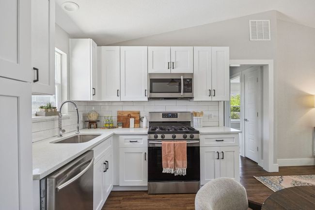 Kitchen featuring stainless steel appliances, vaulted ceiling, tasteful backsplash, white cabinetry, and dark wood-style flooring | Image 16