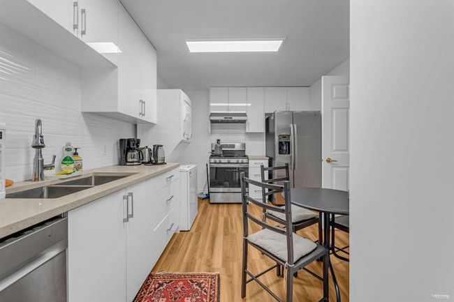 Kitchen featuring stainless steel appliances, under cabinet range hood, white cabinets, and light wood-style flooring | Image 30