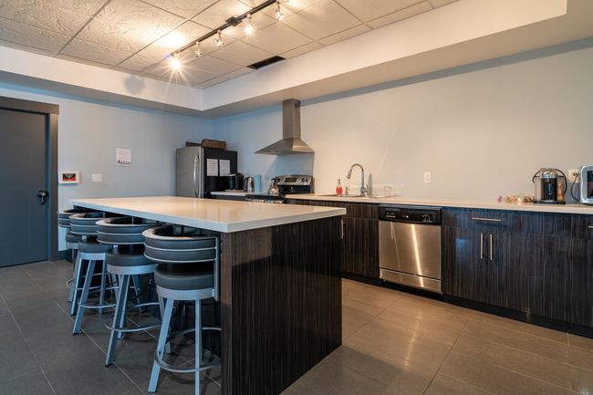 Kitchen featuring stainless steel appliances, wall chimney exhaust hood, a sink, a kitchen bar, and light countertops | Image 15