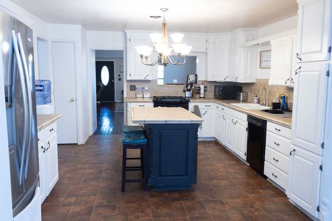 Kitchen with black appliances, a chandelier, a center island, white cabinetry, and tasteful backsplash | Image 7