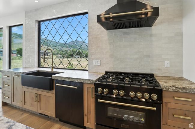 Kitchen featuring black appliances, wall chimney range hood, backsplash, and light wood-style flooring | Image 11