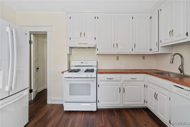 Kitchen with white appliances, a sink, under cabinet range hood, wood finished floors, and white cabinets | Image 19