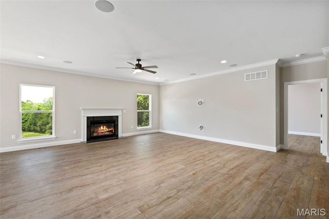 Unfurnished living room featuring wood finished floors, a ceiling fan, a fireplace with flush hearth, baseboards, and crown molding | Image 5