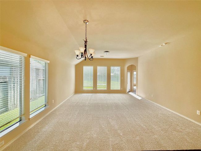 Bright, spacious living area with large windows and neutral carpet, featuring a stylish chandelier and an arched doorway that adds character to the room leading towards the main bedroom. | Image 7
