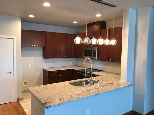 Kitchen featuring stainless steel microwave, a peninsula, a sink, recessed lighting, and light stone countertops | Image 7