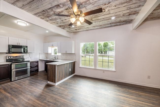Kitchen featuring black microwave, light countertops, wood ceiling, range with two ovens, and a sink | Image 7
