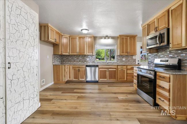 Kitchen with stainless steel appliances, light wood-style floors, decorative backsplash, and a textured ceiling | Image 18