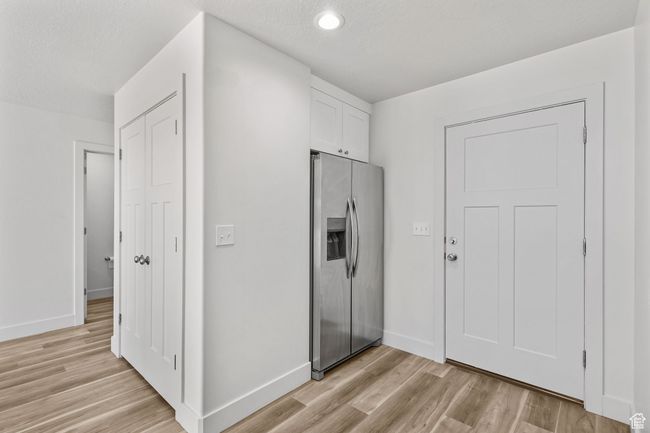 Kitchen featuring stainless steel refrigerator with ice dispenser, light wood finished floors, white cabinetry, baseboards, and recessed lighting | Image 13