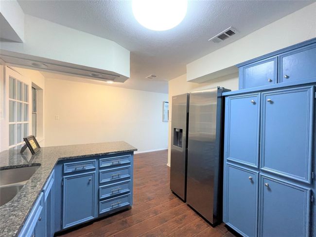 Kitchen with stainless steel fridge, blue cabinets, dark wood-style flooring, a textured ceiling, and dark stone countertops | Image 12