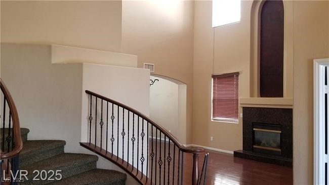 Stairs with a towering ceiling, wood finished floors, a glass covered fireplace, and arched walkways | Image 12