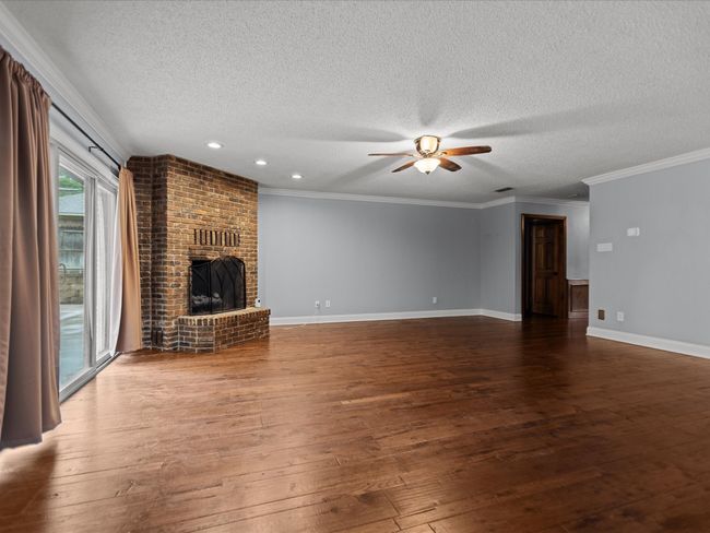Unfurnished living room featuring a textured ceiling, ceiling fan, hardwood / wood-style floors, a brick fireplace, and baseboards | Image 13