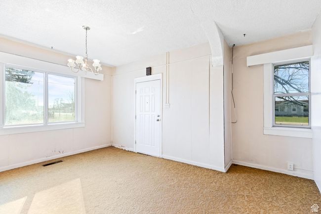 Empty room with a wealth of natural light, a notable chandelier, a textured ceiling, and visible vents | Image 20
