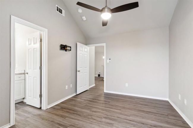 Unfurnished bedroom with lofted ceiling, light wood-type flooring, ensuite bathroom, and ceiling fan | Image 11