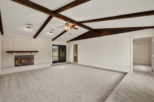 Unfurnished living room featuring lofted ceiling with beams, a fireplace, carpet floors, and a textured ceiling | Image 7