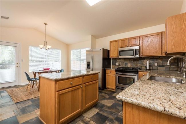 Kitchen featuring appliances with stainless steel finishes, lofted ceiling, backsplash, light stone countertops, and a chandelier | Image 14