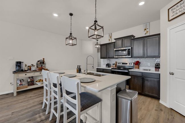 Kitchen featuring stainless steel appliances, light countertops, tasteful backsplash, an island with sink, and light wood-style flooring | Image 11
