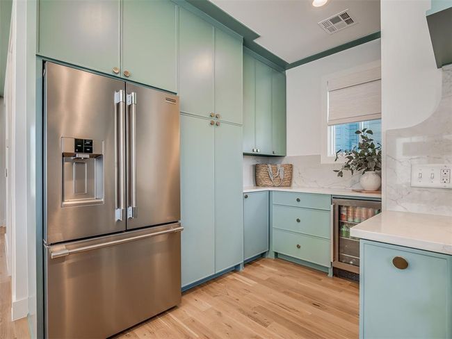 Kitchen with high quality fridge, wine cooler, light wood finished floors, green cabinetry, and light countertops | Image 14