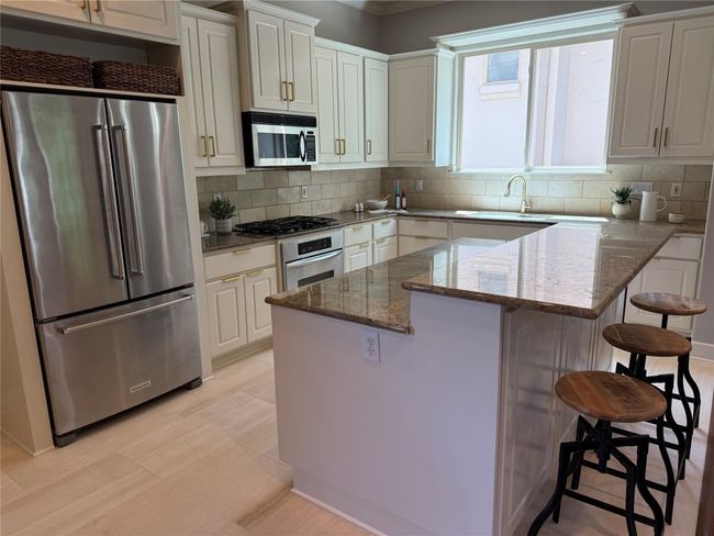 Kitchen with stone counters, appliances with stainless steel finishes, backsplash, and a kitchen bar | Image 16