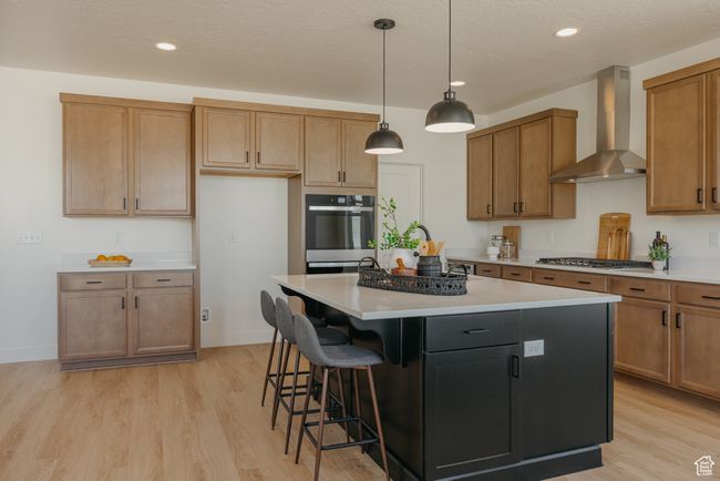 Kitchen featuring wall chimney range hood, a center island, appliances with stainless steel finishes, light countertops, and light wood finished floors | Image 9