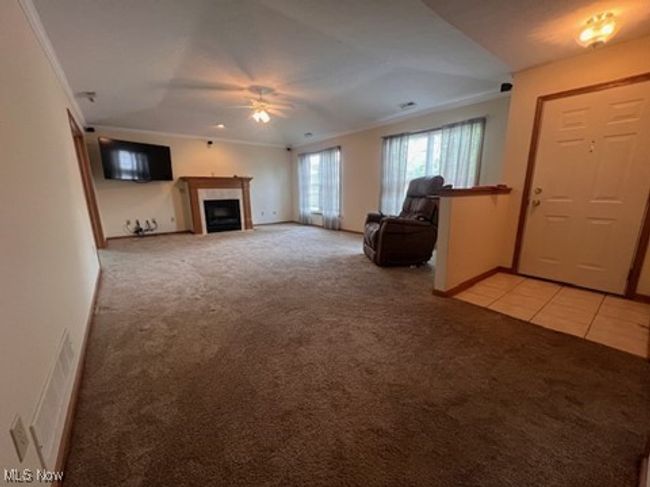 Unfurnished living room featuring light carpet, ornamental molding, ceiling fan, a fireplace, and light tile patterned flooring | Image 6