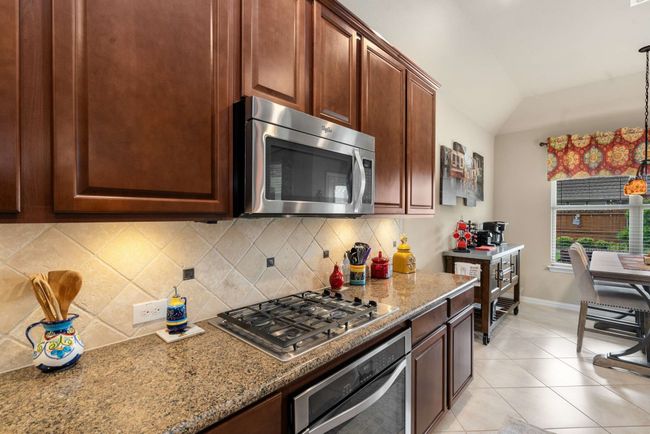 Kitchen with appliances with stainless steel finishes, backsplash, lofted ceiling, and light stone counters | Image 12