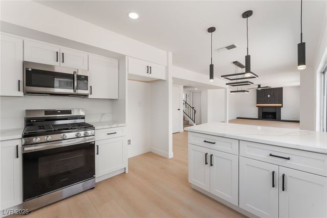 Kitchen with stainless steel appliances, white cabinets, light wood finished floors, light stone counters, and recessed lighting | Image 18