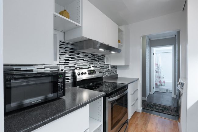 Kitchen featuring decorative backsplash, white cabinets, black microwave, dark countertops, and electric stove | Image 12