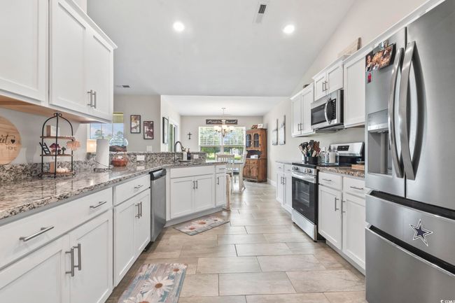 Kitchen with stainless steel appliances, a peninsula, a chandelier, white cabinets, and recessed lighting | Image 13