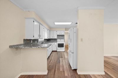 Kitchen with hardwood / wood-style floors, dark stone countertops, white appliances, sink, and white cabinetry | Image 2