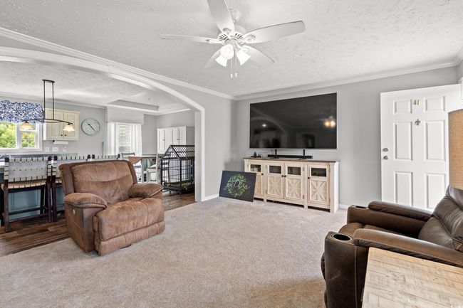 Carpeted living area featuring a textured ceiling, ornamental molding, a ceiling fan, arched walkways, and a chandelier | Image 4
