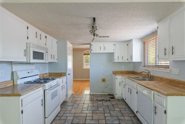 Kitchen with white appliances, a sink, white cabinets, track lighting, and stone finish floors | Image 8