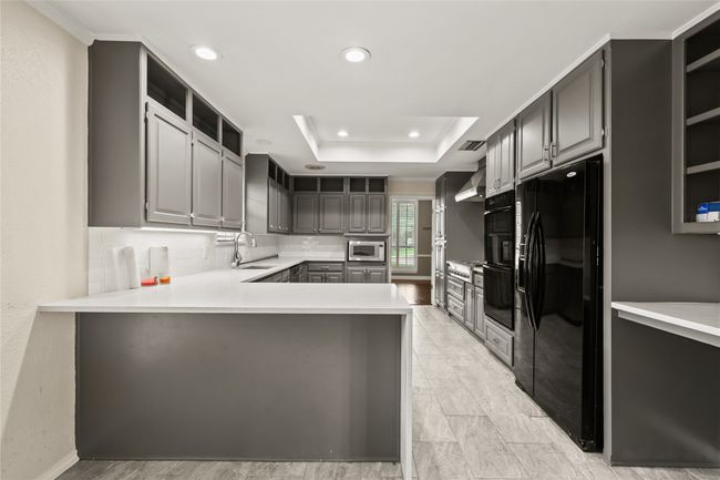 Kitchen featuring black fridge with ice dispenser, stainless steel microwave, gray cabinetry, open shelves, and a peninsula | Image 15