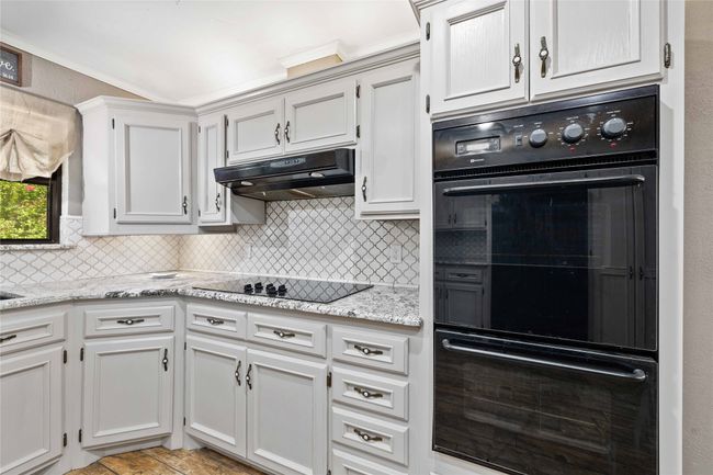 Kitchen with black electric cooktop, under cabinet range hood, backsplash, and granite counters | Image 16