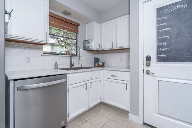 Kitchen featuring stainless steel dishwasher, a sink, light tile patterned flooring, light countertops, and white cabinetry | Image 14