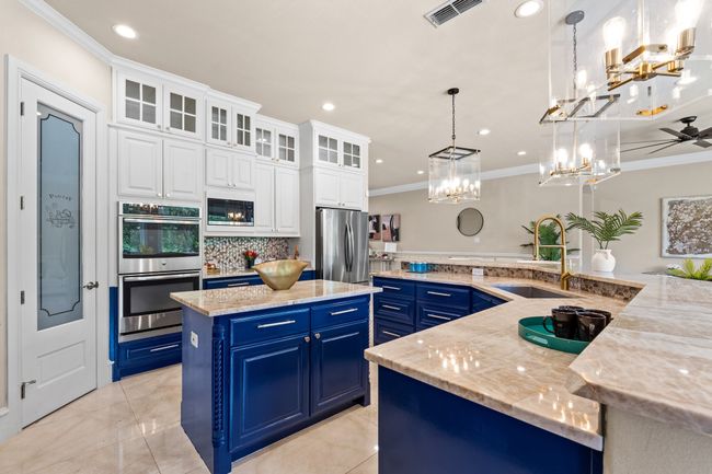 Kitchen with stainless steel appliances, blue cabinets, a large island, crown molding, and a chandelier | Image 8