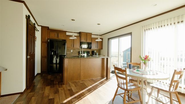 Kitchen featuring brown cabinets, black appliances, ornamental molding, a barn door, and dark wood-style flooring | Image 14