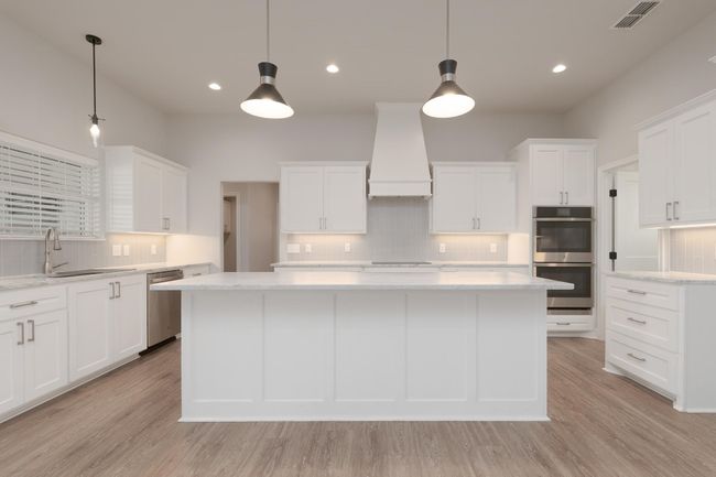 Kitchen featuring custom exhaust hood, appliances with stainless steel finishes, light wood finished floors, and visible vents | Image 9