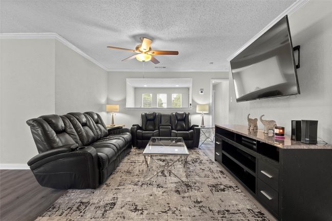 Living area with ceiling fan, a textured ceiling, visible vents, wood finished floors, and ornamental molding | Image 6