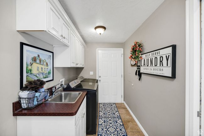 Laundry area featuring a sink, light tile patterned flooring, baseboards, separate washer and dryer, and cabinet space | Image 11
