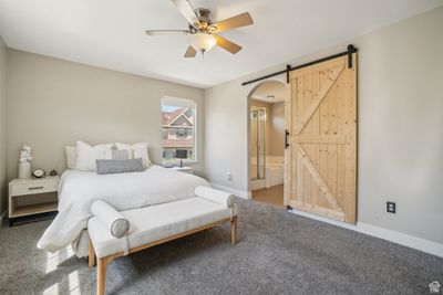 Carpeted bedroom with ensuite bathroom, a barn door, and ceiling fan | Image 1